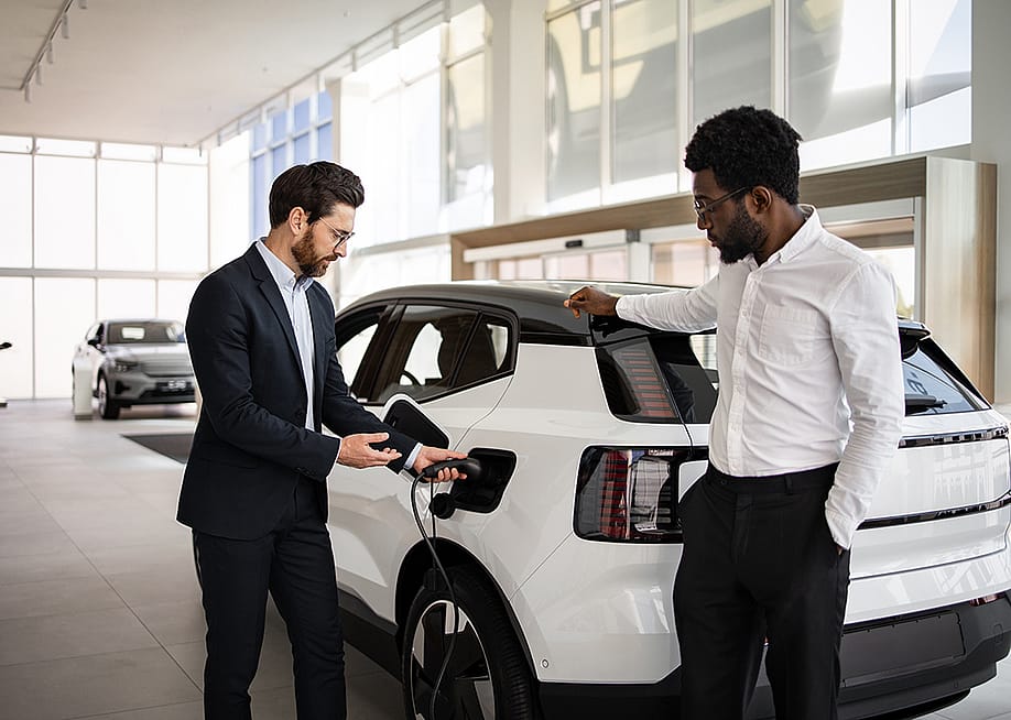 A dealer selling a white electric SUV to businessman in a car dealership. — SofikoS // Shutterstock