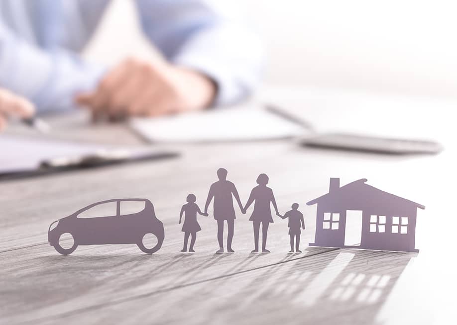 an insurance agent writing in documents with a paper figure of a family with a house and car. — REDPIXEL.PL // Shutterstock