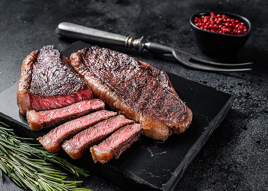 Grilled top sirloin on black marble board, with a sprig of rosemary for decoration, lit from back camera left. — Mironov Vladimir // Shutterstock