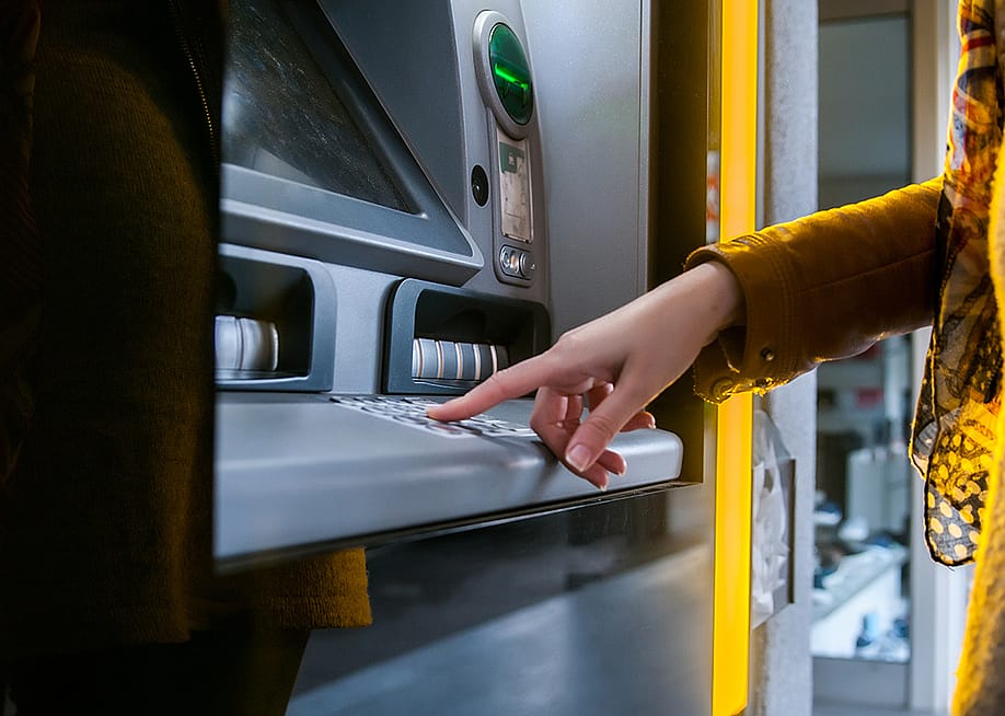 A woman entering info in an ATM to withdraw money. — Dragana Gordic // Shutterstock