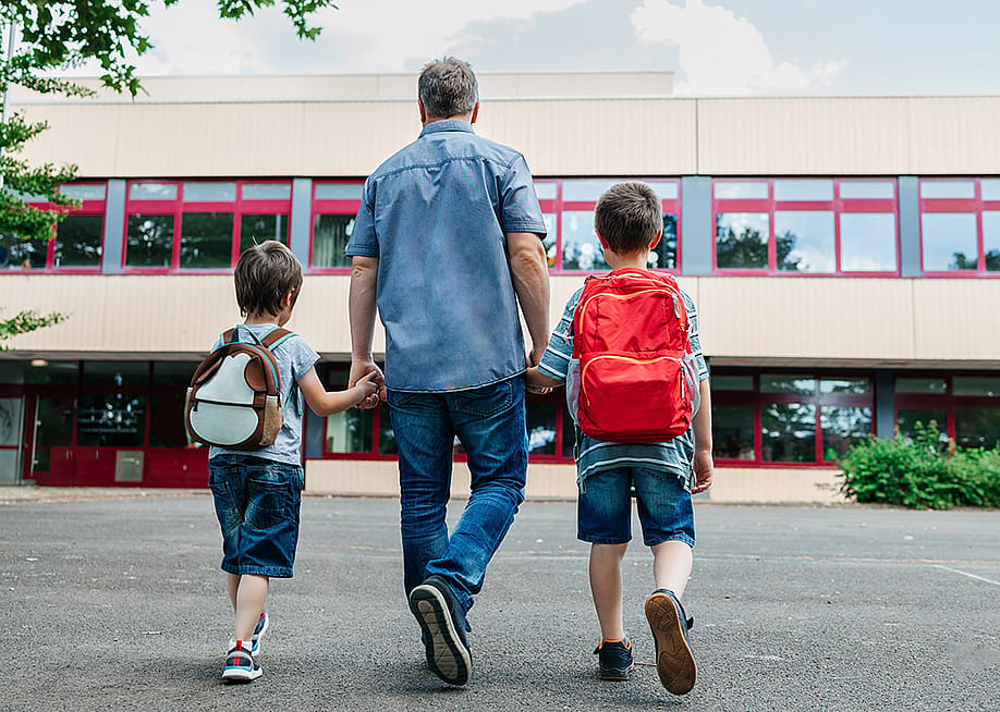 A father holding his two young boys and dropping them back to school. — Elena Medoks // Shutterstock