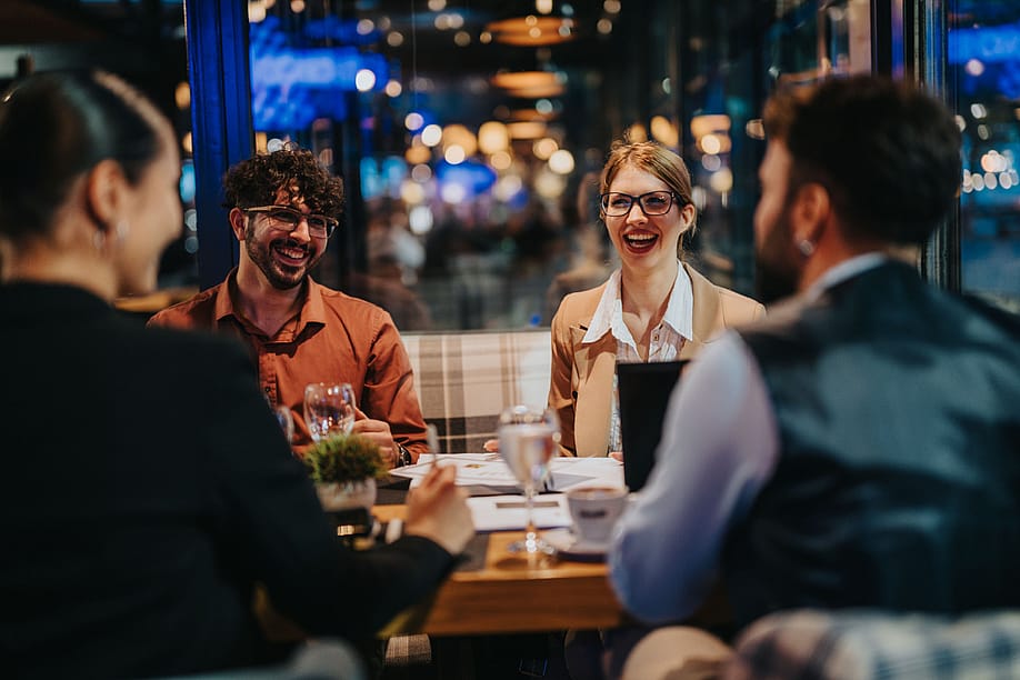 A group of business people laughing and discussing during a meeting in a modern restaurant setting. — Gorgev // Shutterstock