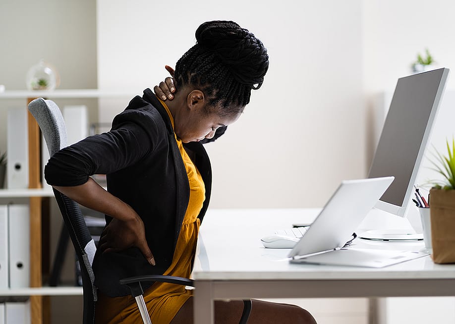 A female employee sitting in her office experiencing back pains. — Andrey_Popov // Shutterstock