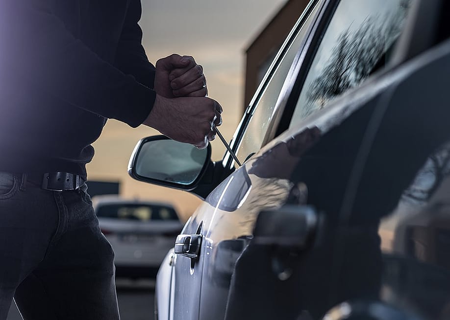 A thief trying to break into a car window with a screwdriver. — Daniel Jedzura // Shutterstock