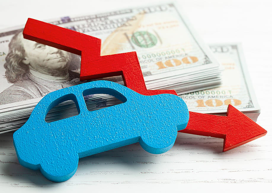 Figure of a car and declining arrow on top of U.S. banknotes. — ADragan // Shutterstock