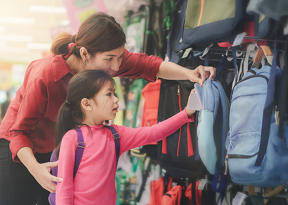 A mother helps her young daughter to pick a new bag for school at a store. — Chanintorn.v // Shutterstoc