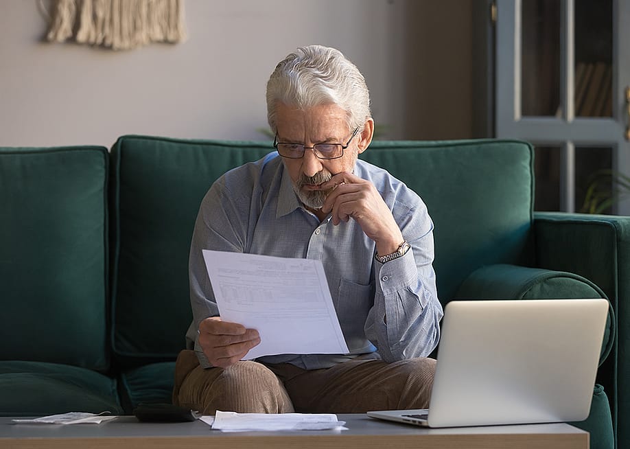 A senior man sitting on a couch intensely analyzing an expense bill. — fizkes // Shutterstock