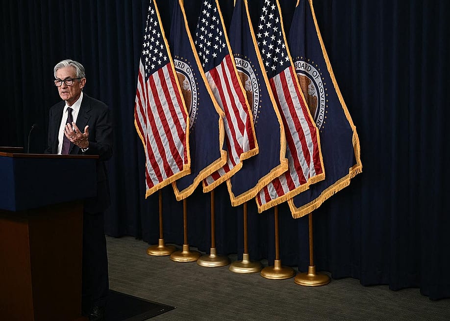 Fed chair Jerome Powell speaking at a podium with six flags behind him, 3 U.S. flags and 3 Board of Governors flags in alternating pattern. — BRENDAN SMIALOWSKI // AFP via Getty Images