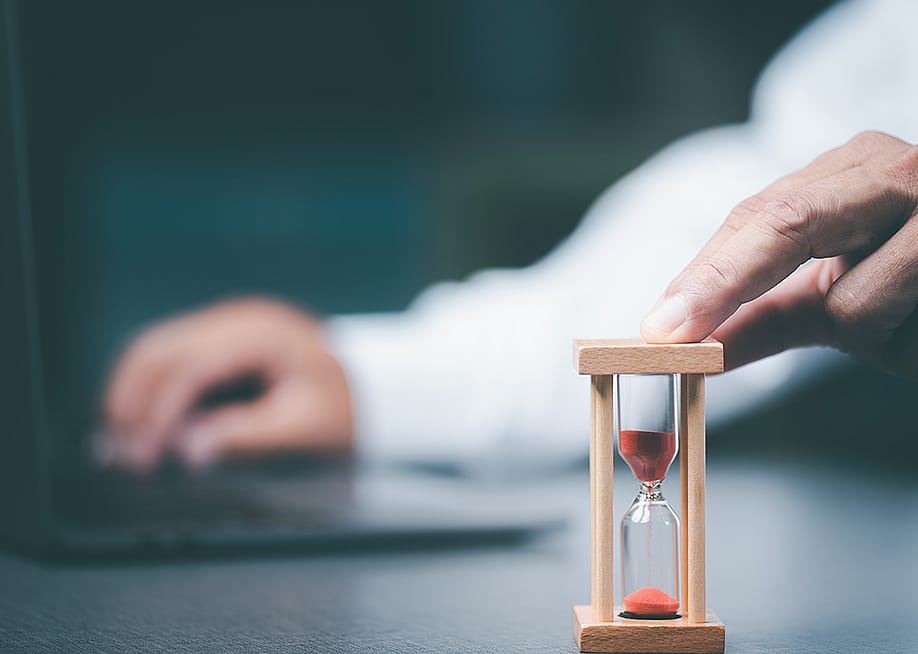 A business employee using a small time hourglass beside a laptop. — chaylek // Shutterstock