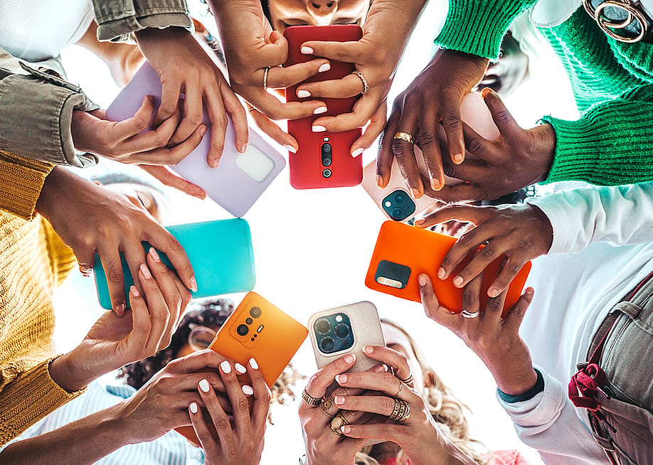 A group of young people using their smartphones outside while forming a circle. — DavideAngelini // Shutterstock