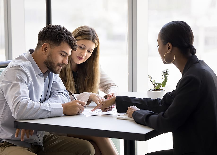 A realtor guiding a couple on signing a property contract. — fizkes // Shutterstock