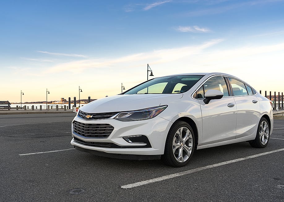 A white 2017 Chevrolet Cruz on a parking lot near seaside. — Victor Maschek // Shutterstock