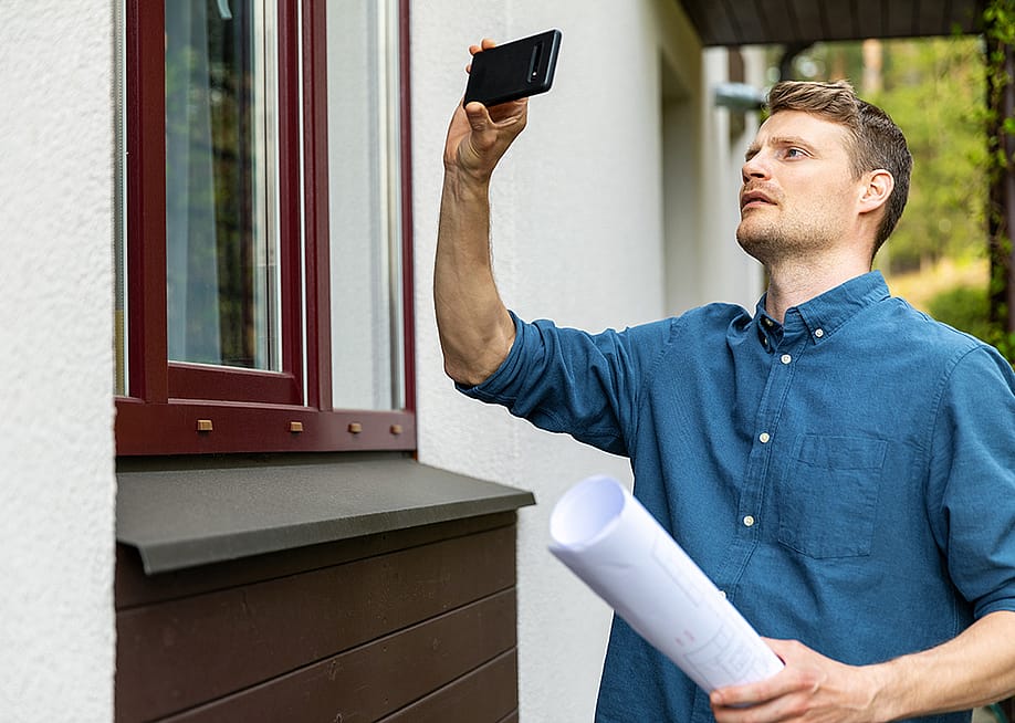 A real estate appraiser takes photo of the outside of a property with his phone. — ronstik // Shutterstock
