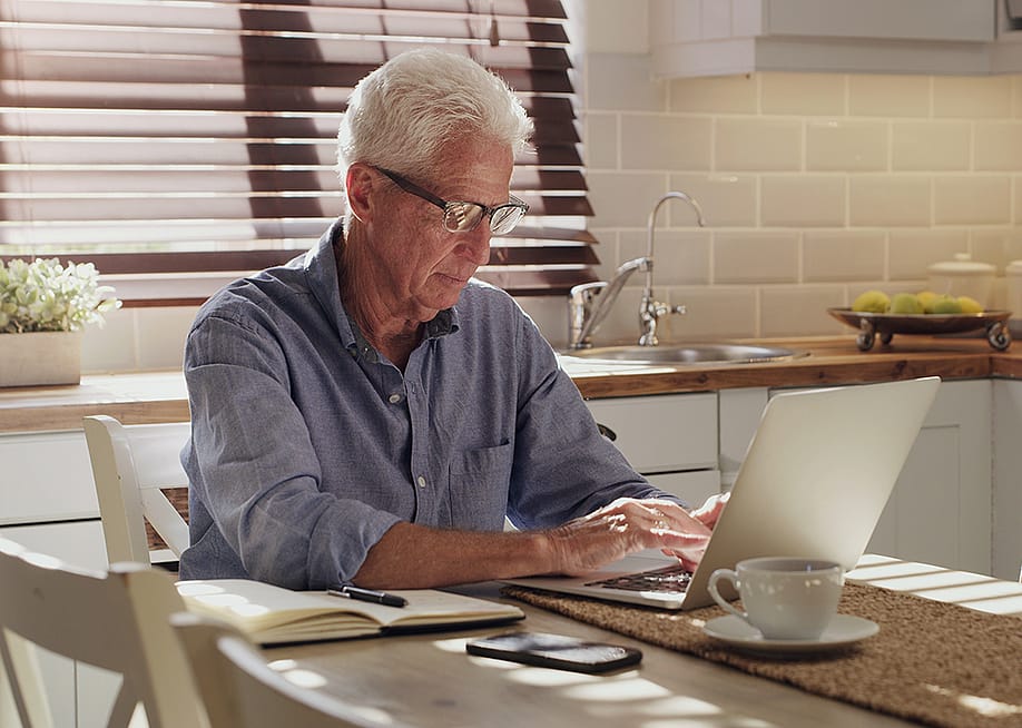 A senior man using a laptop in his kitchen. — PeopleImages // Shutterstock