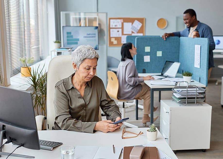 A senior businesswoman working at her desk in an open office setting. — SeventyFour // Shutterstock