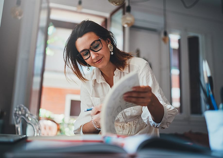 A freelance female designer browsing her design book in a studio. — ImYanis // Shutterstock