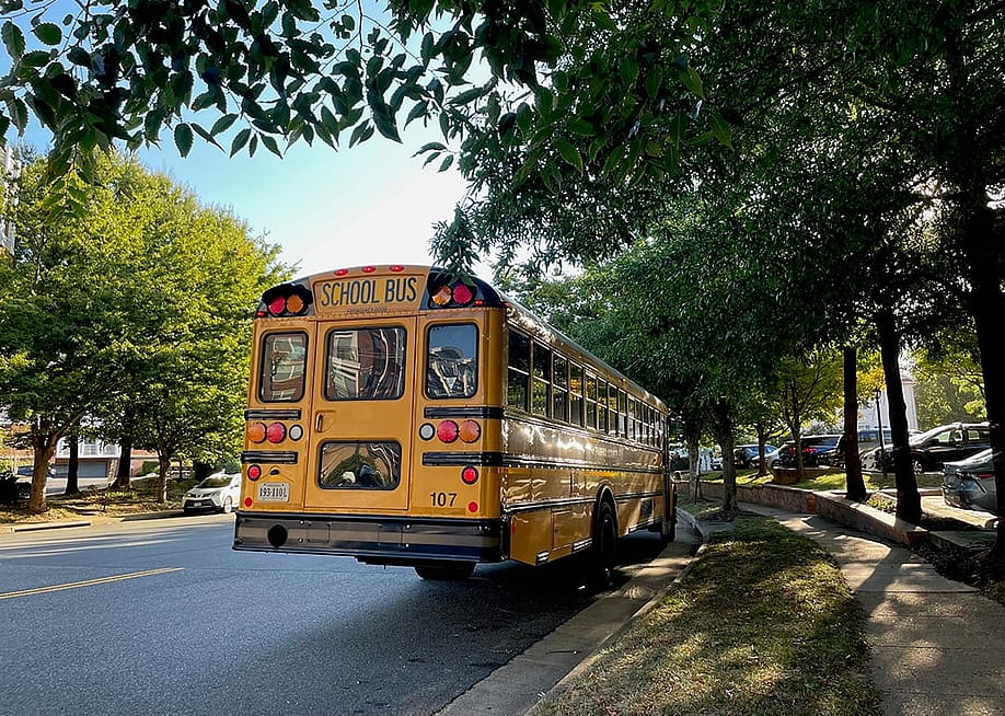 A yellow school bus waits by a bus stop in a family neighborhood in Fairfax County, Virginia. — Equator Aesthetics // Shutterstock