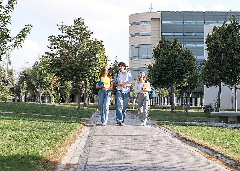 A group of three young college students chatting while walking on university campus footpath. — Daniel Megias // Shutterstock