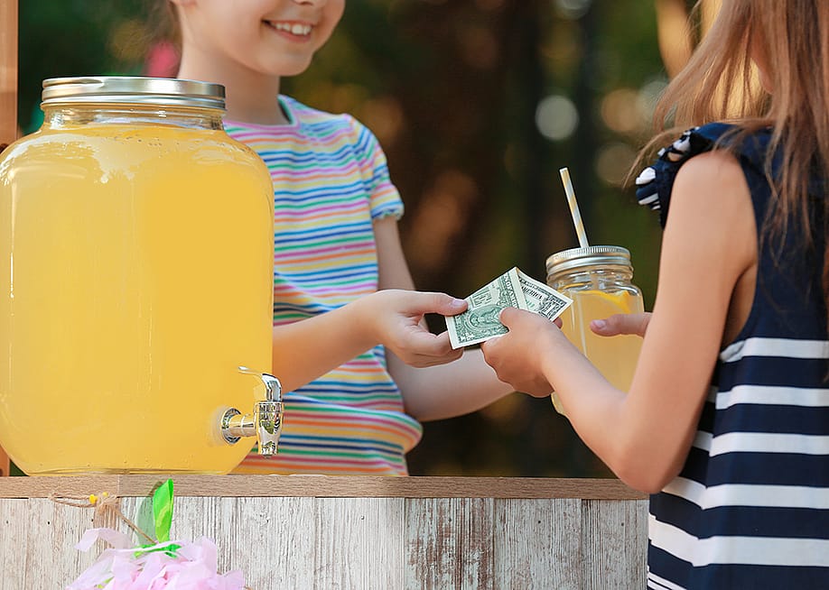 A young girl sells lemonade to another young girl at the park. — New Africa // Shutterstock