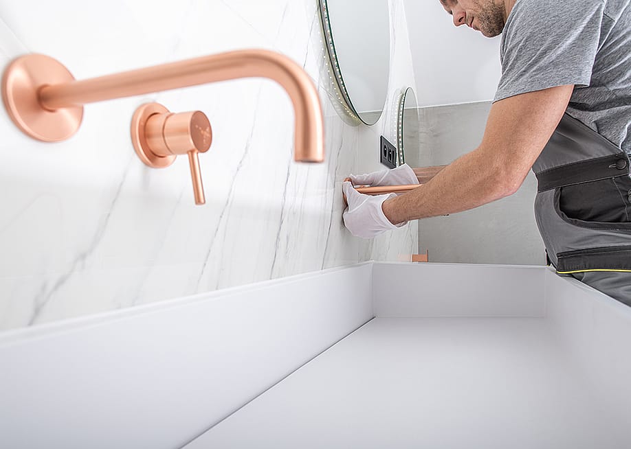 A handyman installs copper faucet to a modern marble wall bathroom. — Virrage Images // Shutterstock