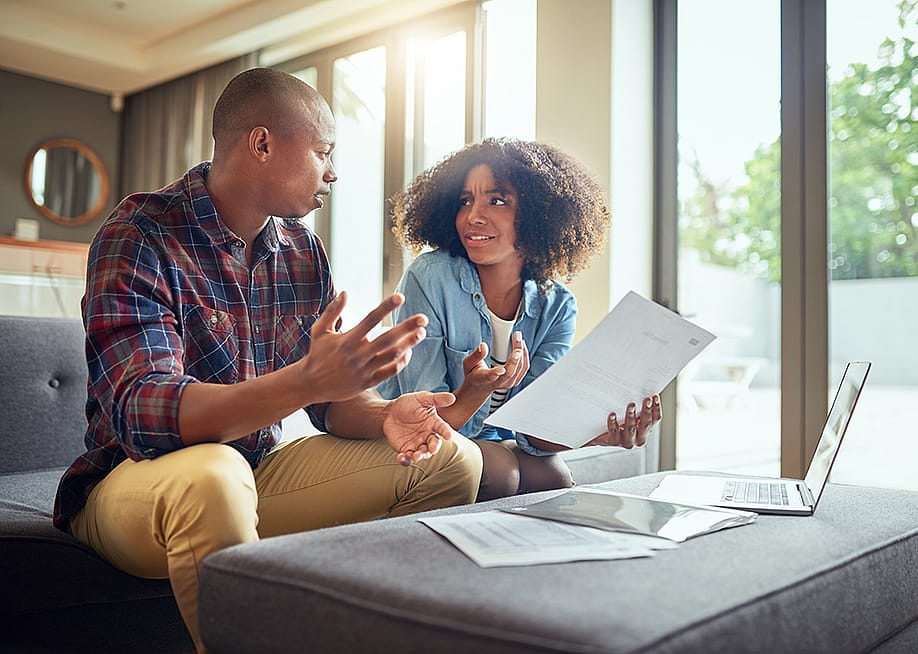 A young couple discussing finances while holding paperwork. — PeopleImages // Shutterstock