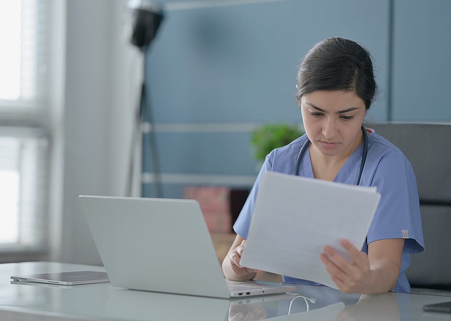 A female nurse reading documents in an office. — Zmaster // Shutterstock