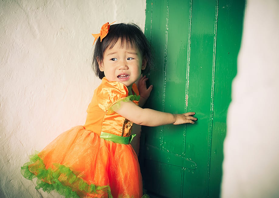 A young girl wearing an orange Halloween dress crying during a party. — Mcimage // Shutterstock