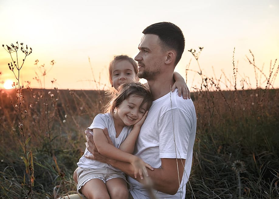 A father with her two young daughters out on a grass field during sunset. — PV productions // Shutterstock