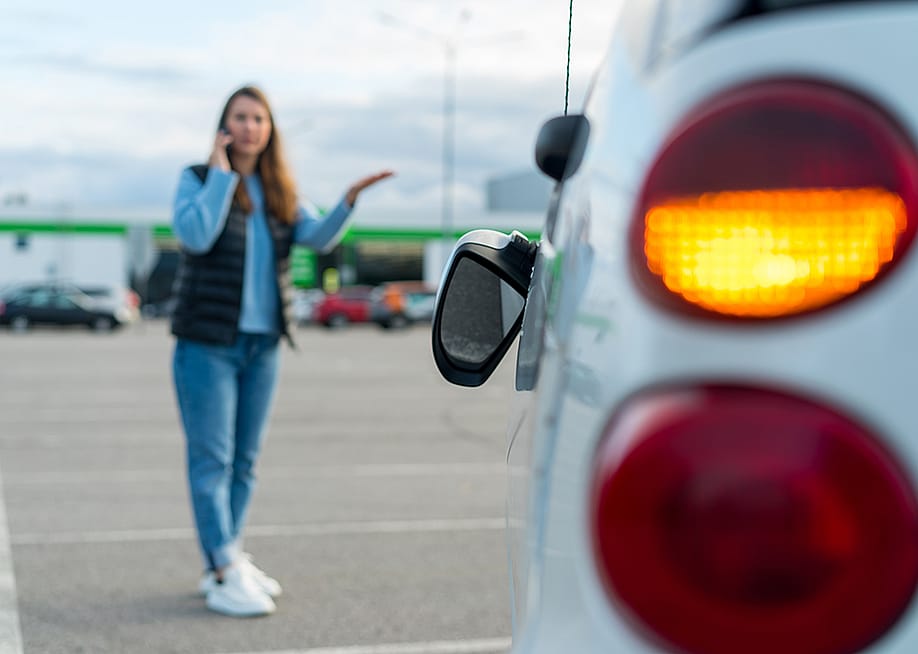 Woman talking on her phone while looking at her car's broken left side rear-view mirror. — vimpro // Shutterstock