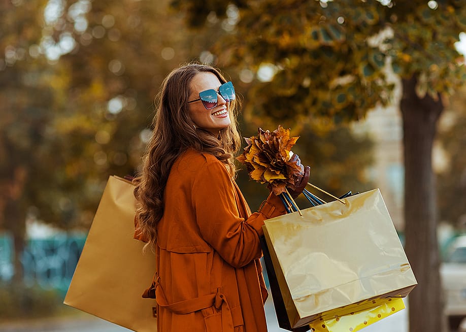 A happy stylish woman holding shopping bags and autumn leaves. — Alliance Images // Shutterstock