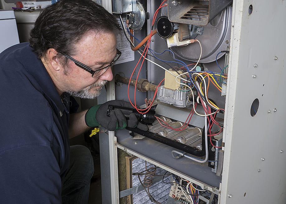 A technician inspects a gas furnace before its cleaning. — Indy Edge // Shutterstock