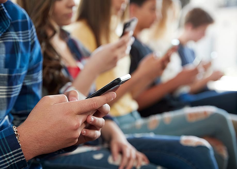 A row of high school students using mobile phones. — Monkey Business Images // Shutterstock