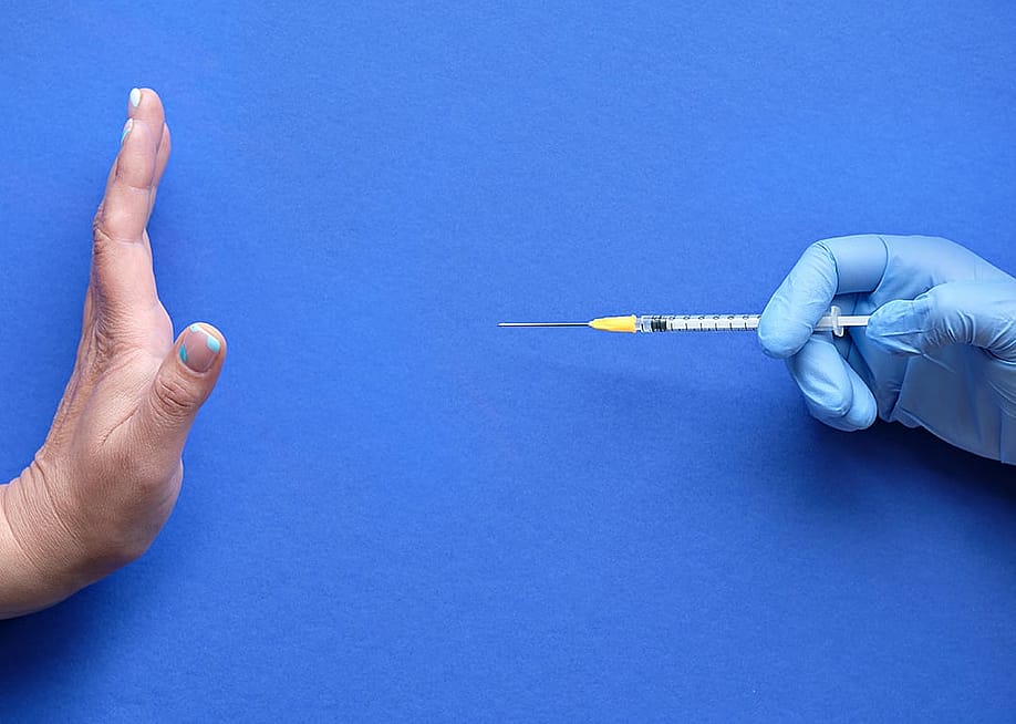A hand refusing to receive a vaccine syringe. — tilialucida // Shutterstock