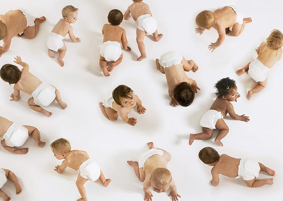 A group of diverse babies crawling on a white floor. — sirtravelalot // Shutterstock