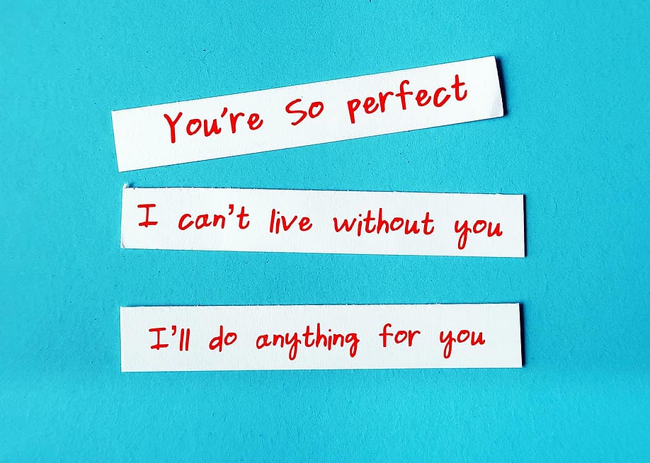 Love bombing messages written on slips of paper such as "I can't live without you," photographed against turquoise background. — Ariya J // Shutterstock