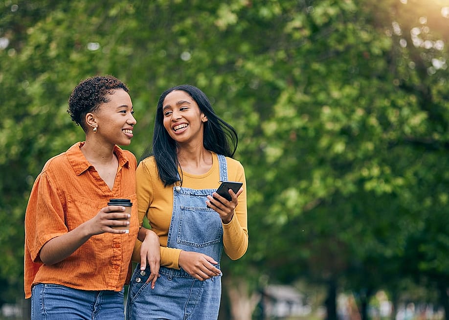 Two women having coffee while walking in a park. — PeopleImages // Shutterstock