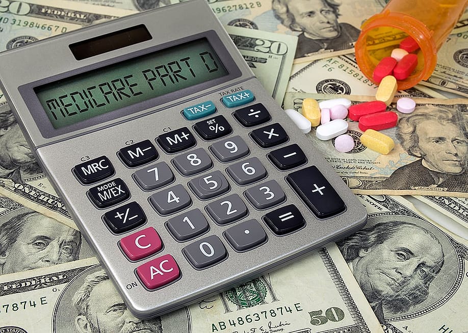 Medicare Part D text on a calculator with prescription pills spilling from bottle on top of US banknotes. — Maria Dryfhout // Shutterstock