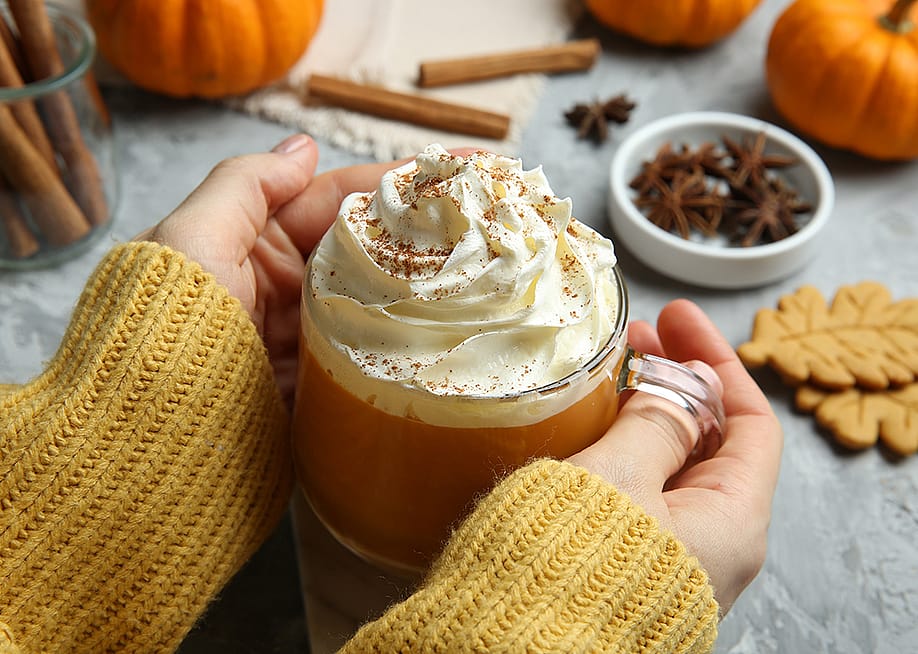 Closeup on a woman holding a cup of pumpkin spice latte with whipped cream. — New Africa // Shutterstock