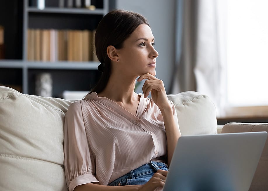 A young woman at home contemplating on couch while using laptop. — fizkes // Shutterstock