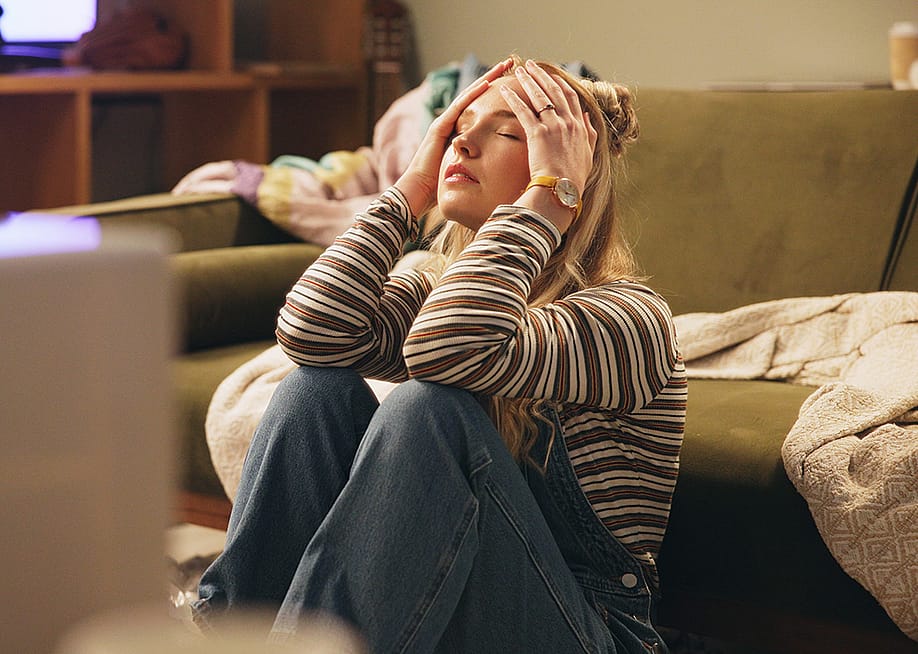 A stressed young woman sitting on the floor holding her head. — PeopleImages // Shutterstock