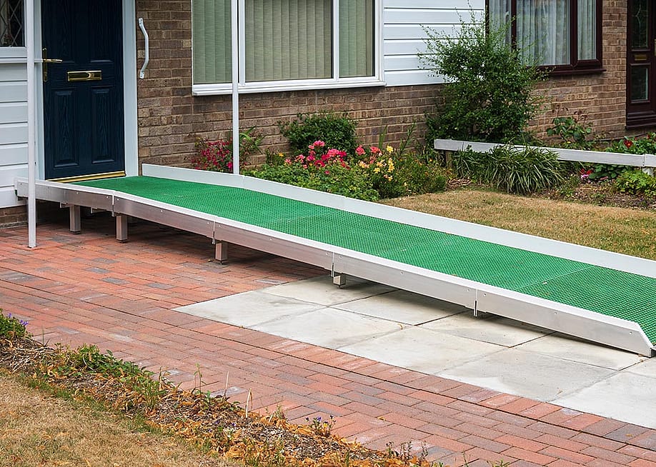 A wheelchair access ramp with green plastic surface installed at the door to a building that has a single step up to a black door. — Nimur // Shutterstock