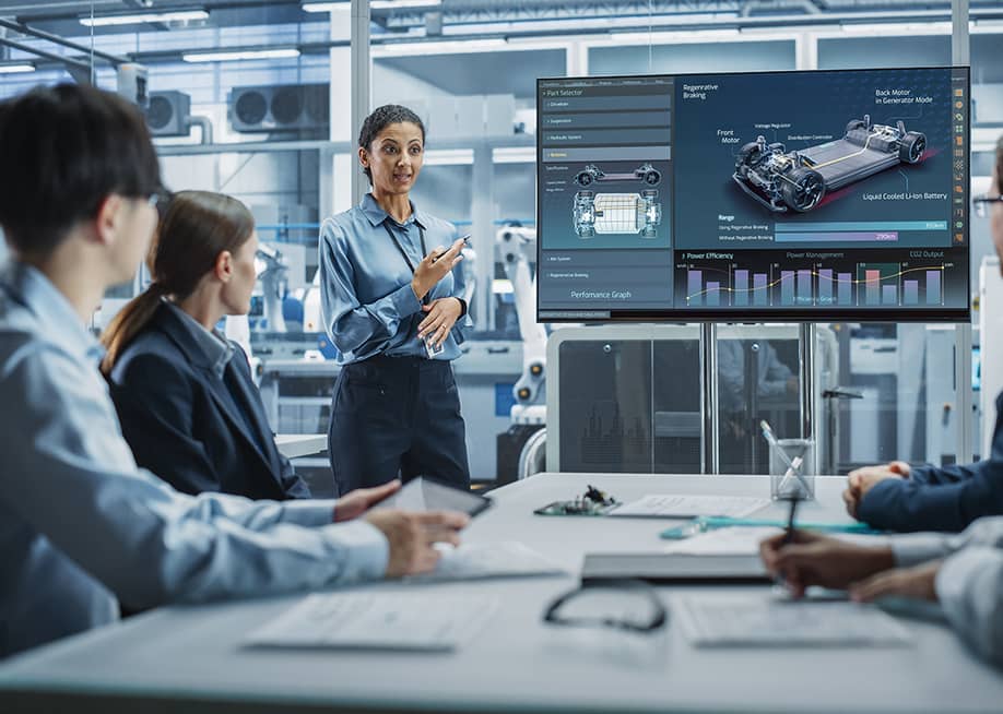 A female project manager leads her team of engineers with a presentation of a new car model in an EV manufacturing facility office. — Gorodenkoff // Shutterstock