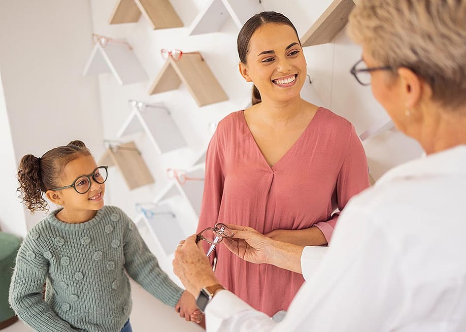 Girl with mother trying on glasses at an eyewear store talking to specialist. — PeopleImages // Shutterstock