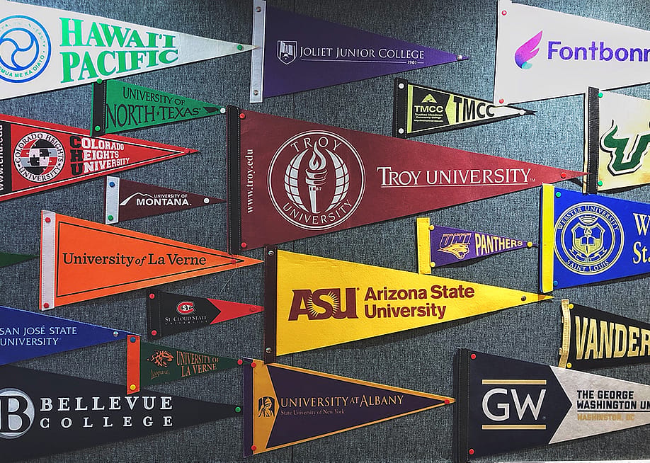 Pennant flags of US colleges and universities on a wall. — Red Herring // Shutterstock
