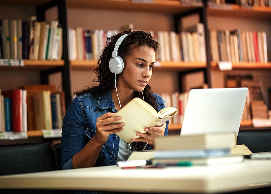 A fema collge student reading a book in a library while listening to music. — BalanceFormCreative // Shutterstock