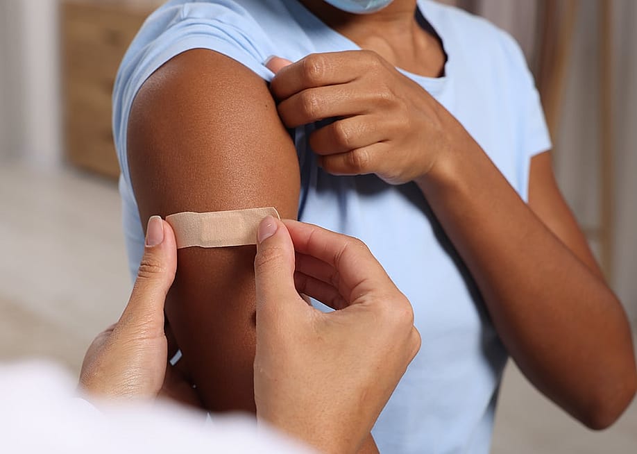 A doctor puts adhesive bandage on a woman's arm after vaccination. — New Africa // Shutterstock