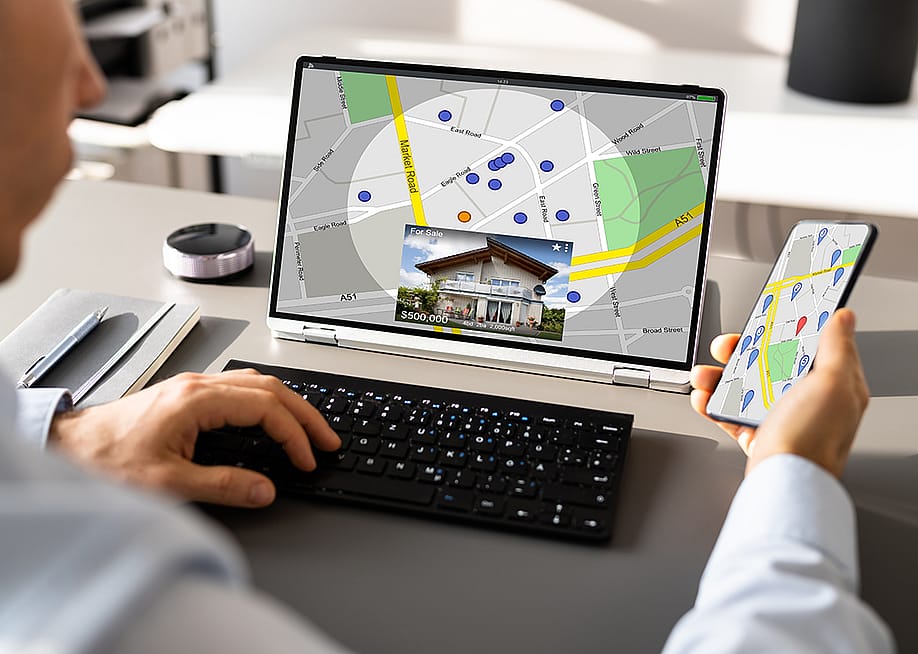 Person looking up a map view of a property's location using a laptop and a phone. — Andrey_Popov // Shutterstock