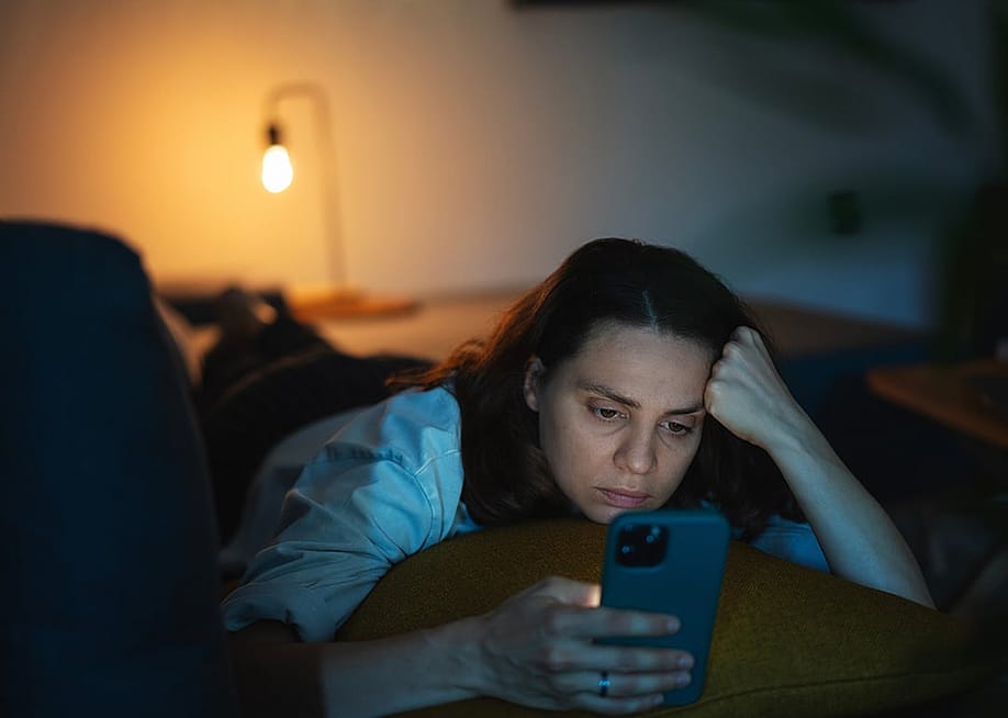 A serious young woman lying on a sofa and scrolling through her phone. — Olezzo // Shutterstock