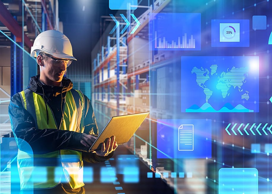 A male worker using laptop in a warehouse with an overlay of technology and logistics graphics. — FOTOGRIN // Shutterstock