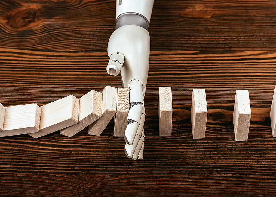 A robotic hand prevents wooden domino blocks from falling midway. — LightField Studios // Shutterstock